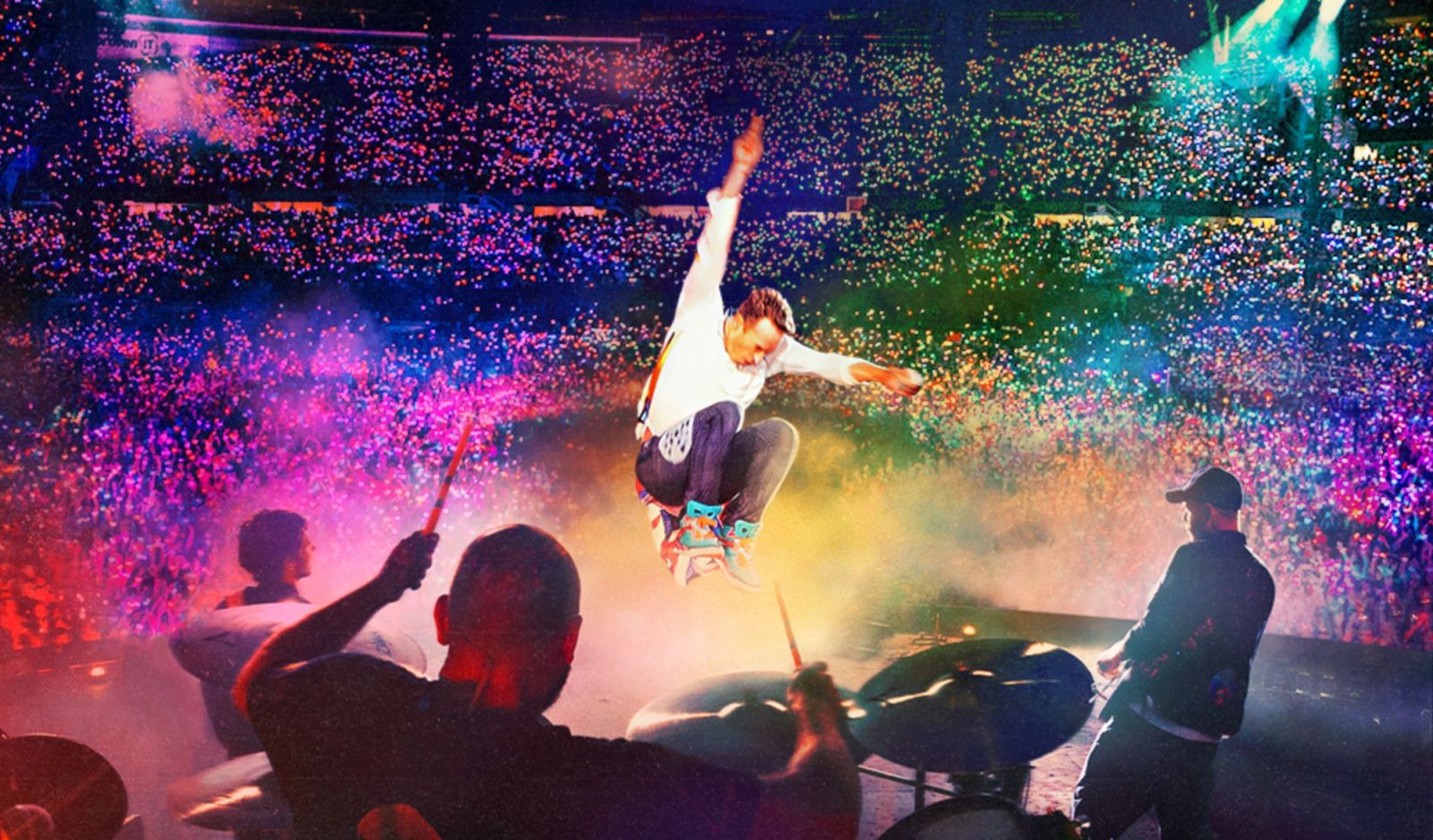 coldplay performing at their concert with a rainbow of lights in the background
